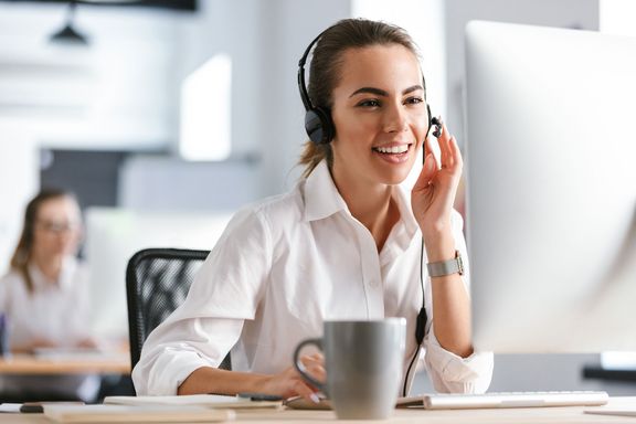 Eine junge Frau sitzt mit einem Headset vor einem Computer im Büro eines Callcenters.